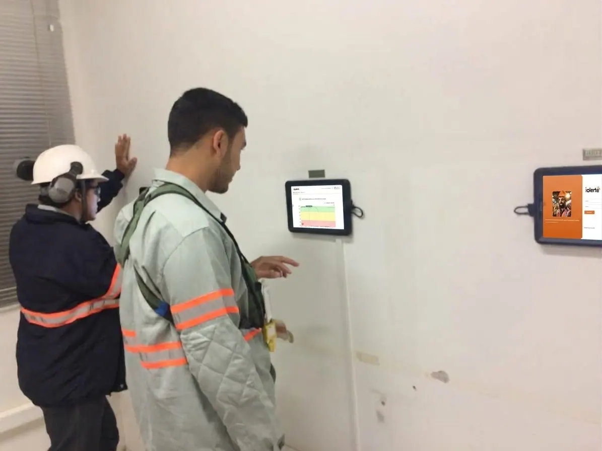 Dois trabalhadores diante de um tablet do iAlerta fixado na parede